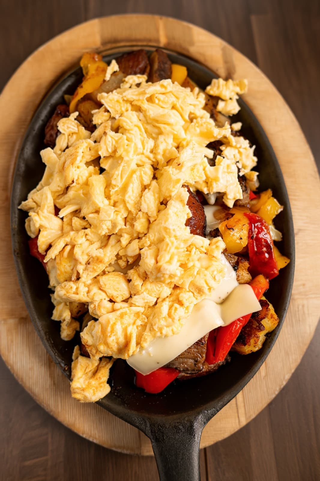 Sunnyside Cafe signature steak skillet — fluffy scrambled eggs piled over seared steak, melted provolone, roasted peppers, onions, and crispy potatoes in a cast-iron pan